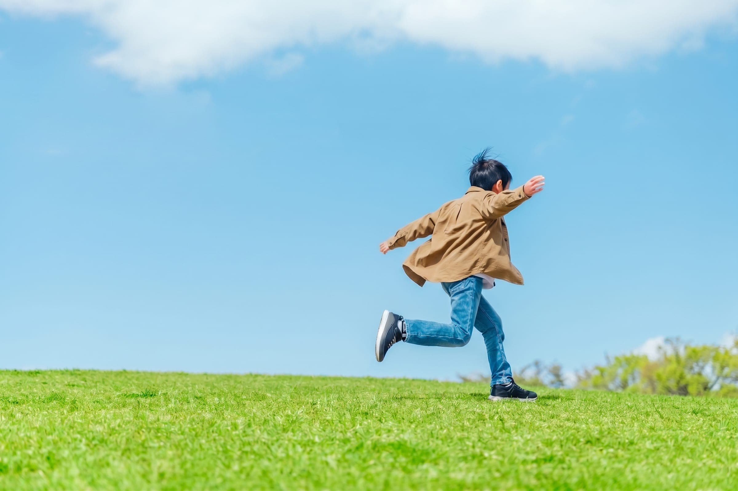 青空の下、草原を駆けていくお子さん